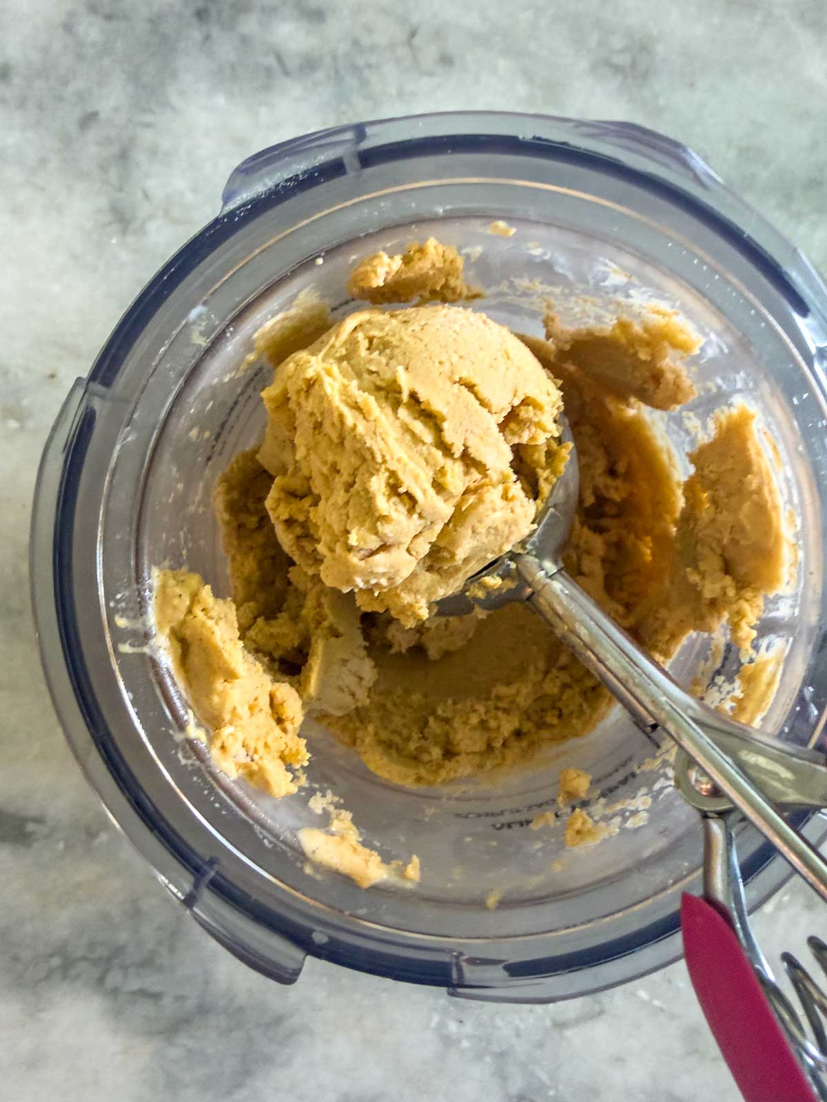 A creami container with ice cream being scooped out using a metal ice cream scooper, placed on a marble countertop—perfect for pairing with a homemade batch of Ninja Creami Pumpkin Ice Cream.
