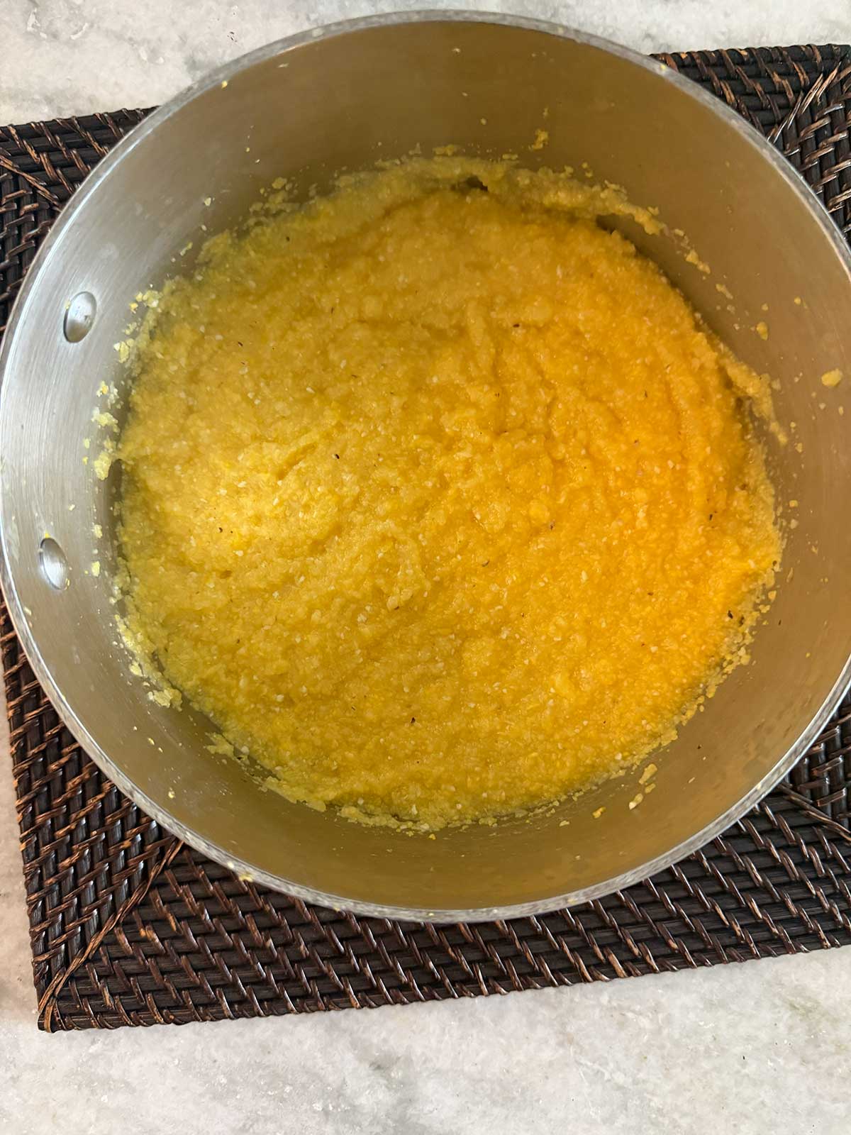 A pot filled with yellow grits sits on a dark woven placemat atop a light-colored countertop.