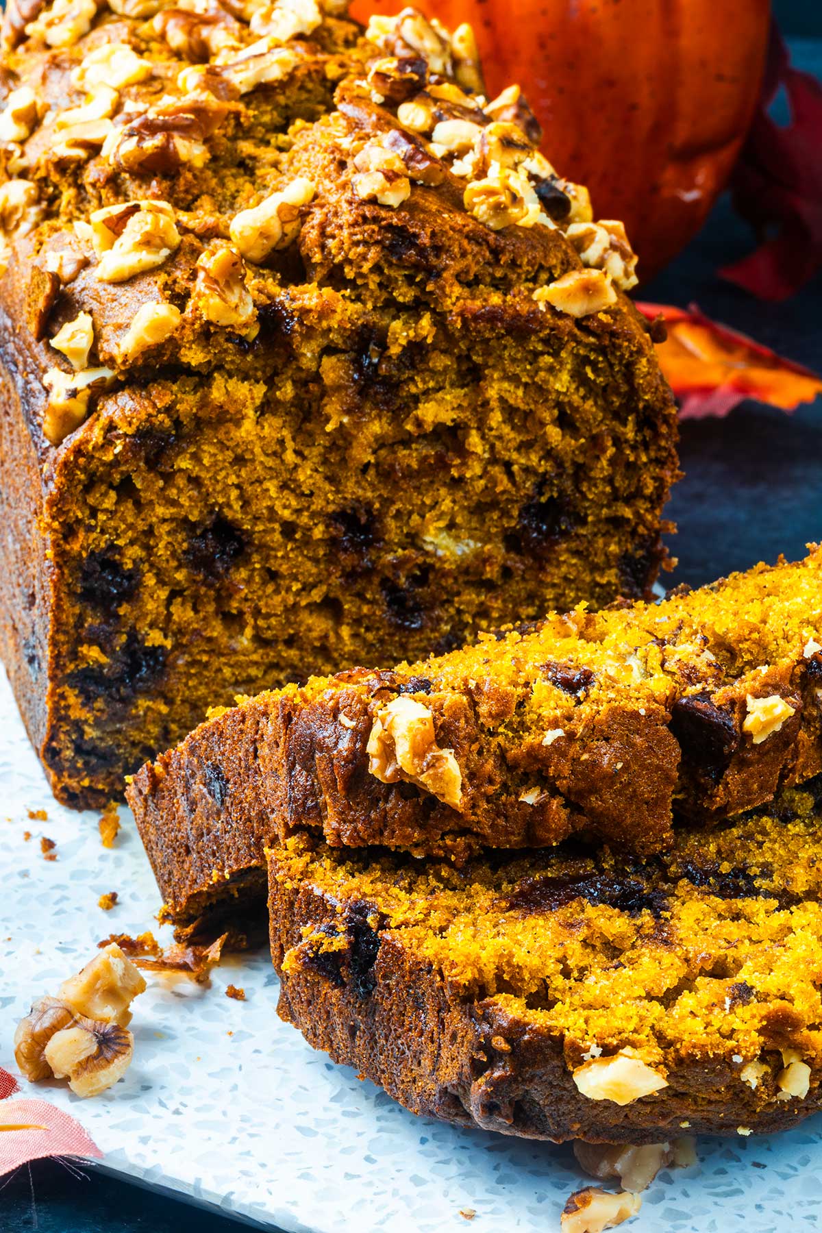 Sliced pumpkin bread with chocolate chips and chopped walnuts on top, displayed on a white platter. The bread has a moist, golden-orange crumb and a rustic texture.