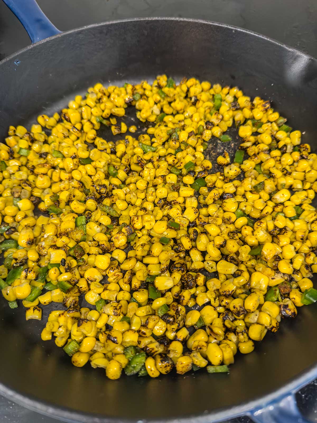 Charred corn kernels and chopped green peppers cooking in a black skillet, perfect for adding bold flavor to a street corn chicken rice bowl, with some pieces showing browned, crispy edges.