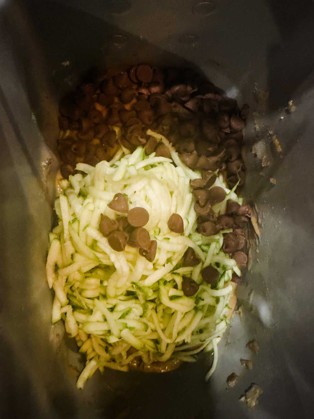 Shredded zucchini and chocolate chips inside a dark mixing bowl, ready to be combined.