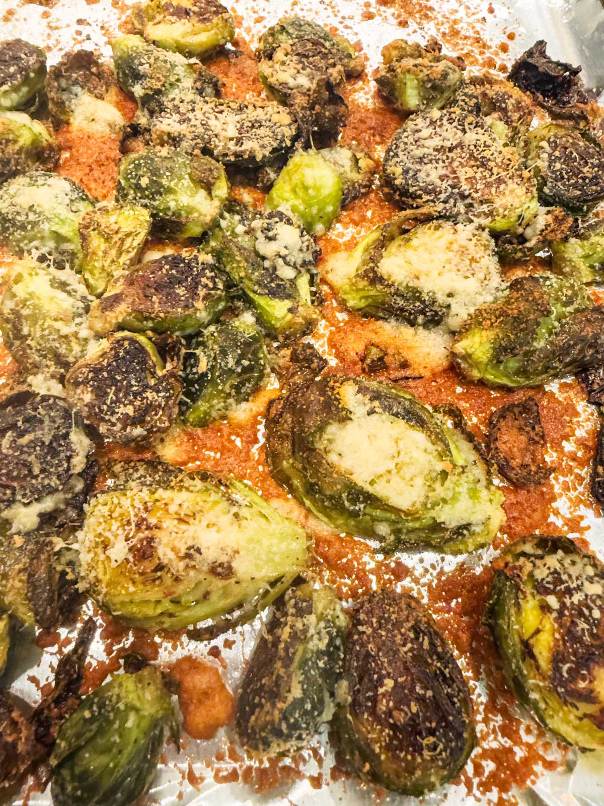 Garlic parmesan Brussels sprouts roasted to perfection, topped with melted cheese and seasoning, displayed on a foil-lined baking sheet.