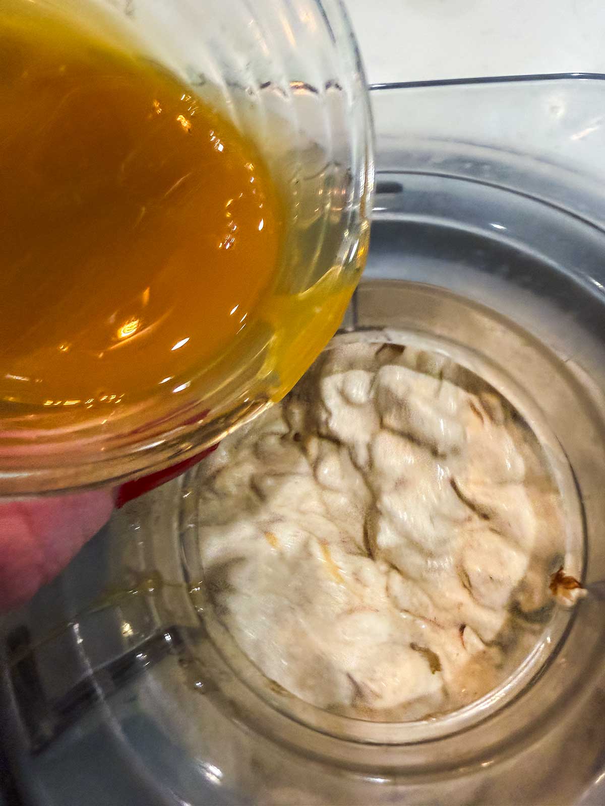 A glass bowl pours orange liquid into an ice cream maker containing partially churned ice cream mixture.
