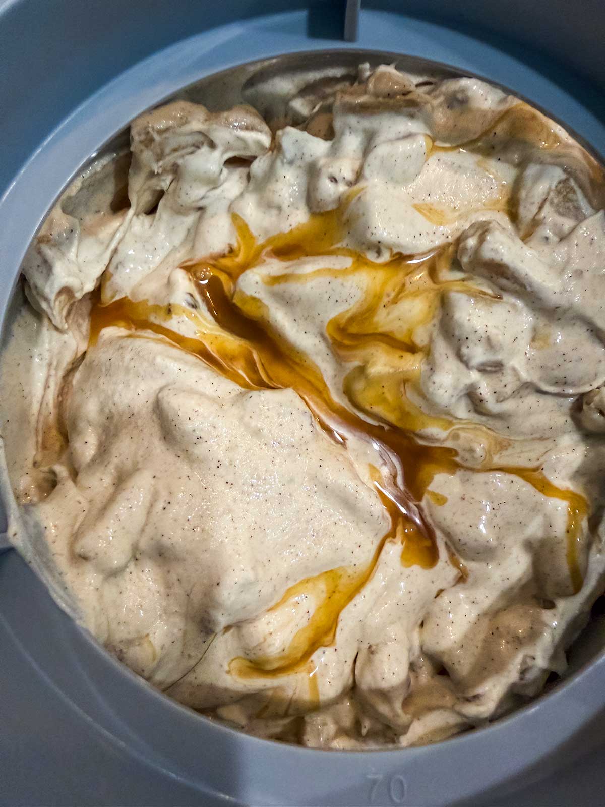 Creamy brown ice cream with visible specks and swirls of caramel sauce on top, inside a gray mixing container.
