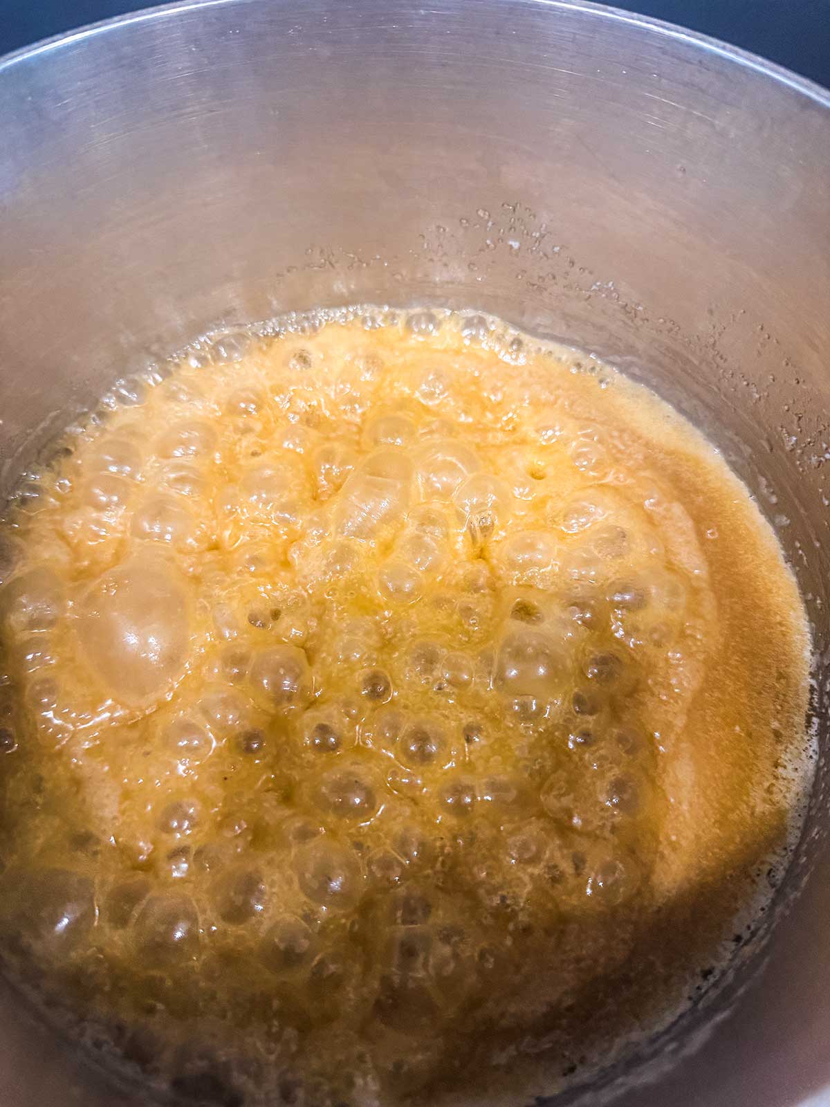 Golden brown sugar syrup bubbling in a metal pot, showing the caramelization process as it cooks on the stove.