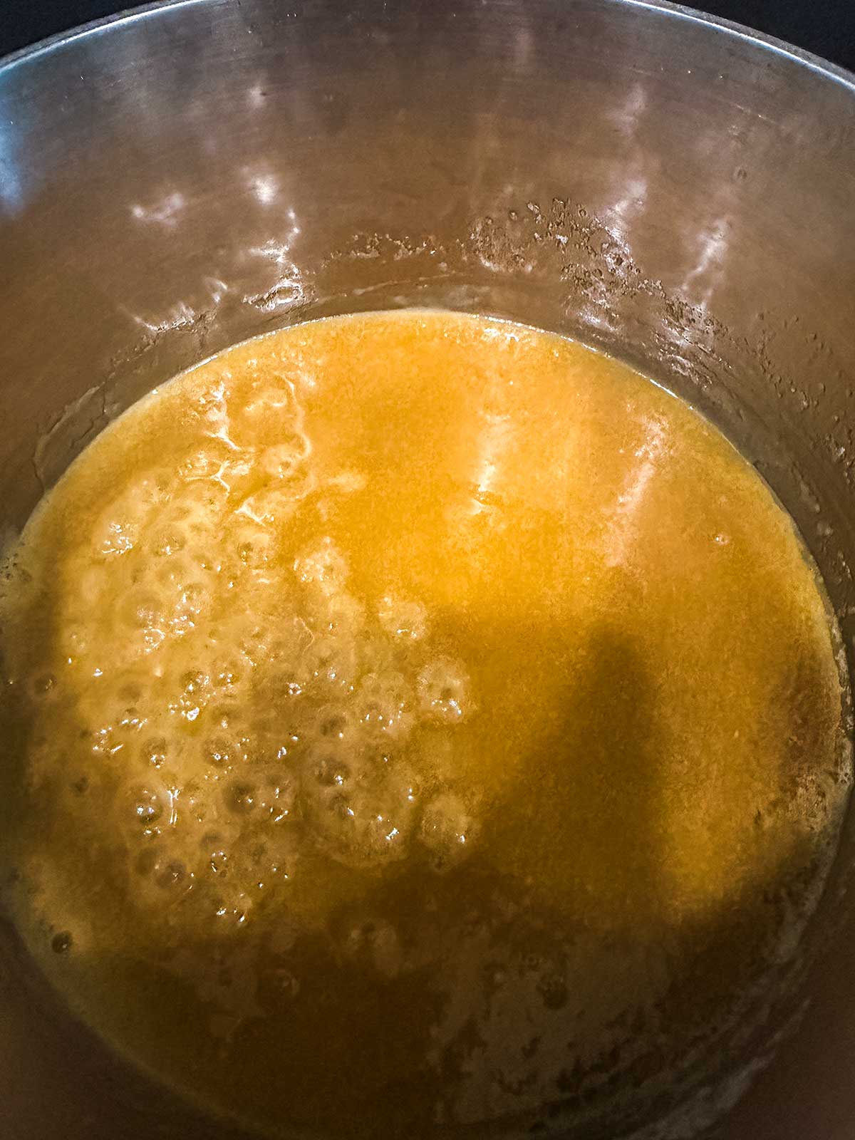 A close-up of a pot with golden melted butter or caramel bubbling and simmering inside.