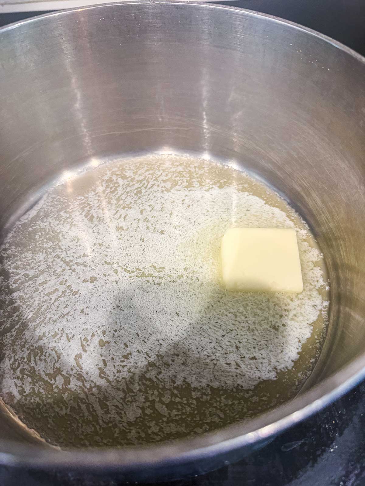 A metal pot with a partially melted square of butter surrounded by liquid butter.