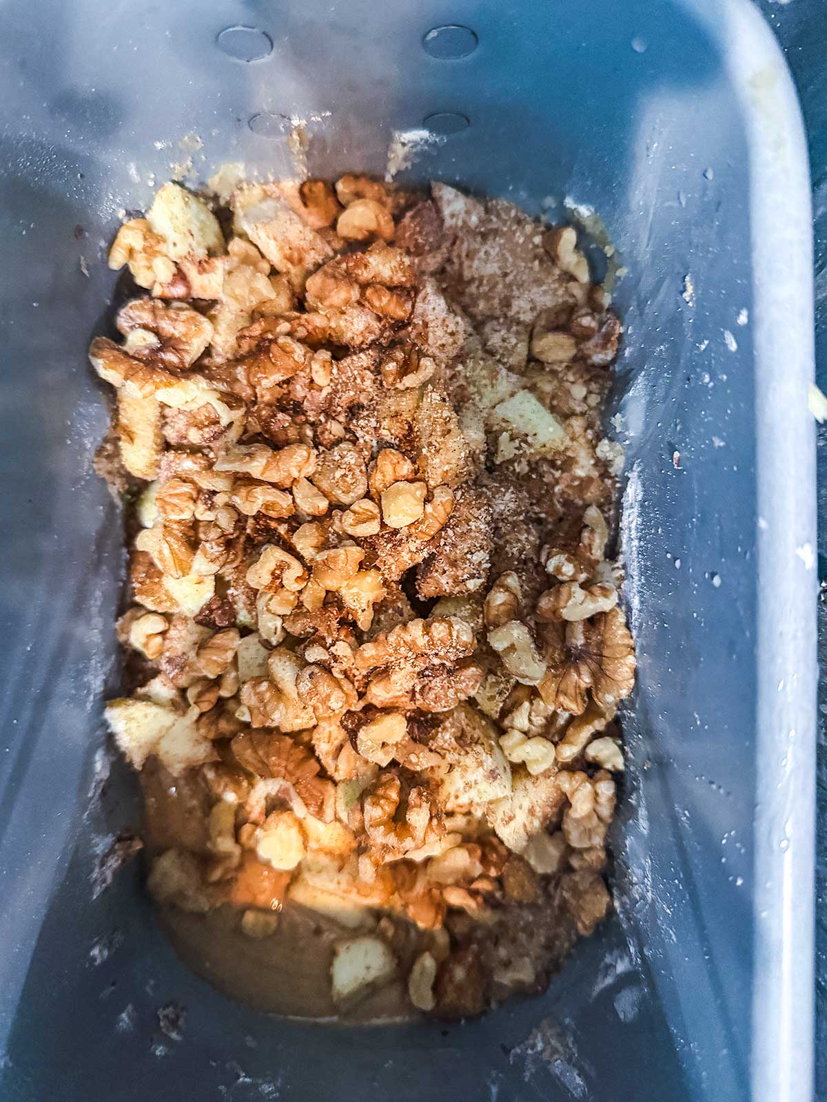 Chopped walnuts, apples, and cinnamon are mixed together in a gray baking pan, ready to be baked.