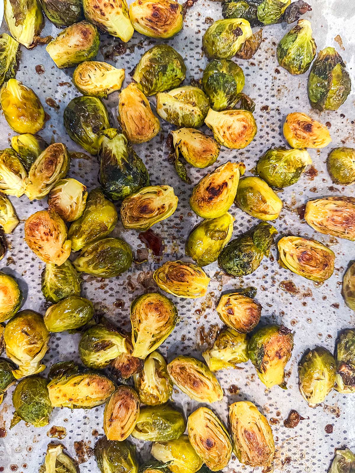 Roasted Brussels sprouts sliced in half, browned and crispy, scattered across a parchment-lined baking sheet.