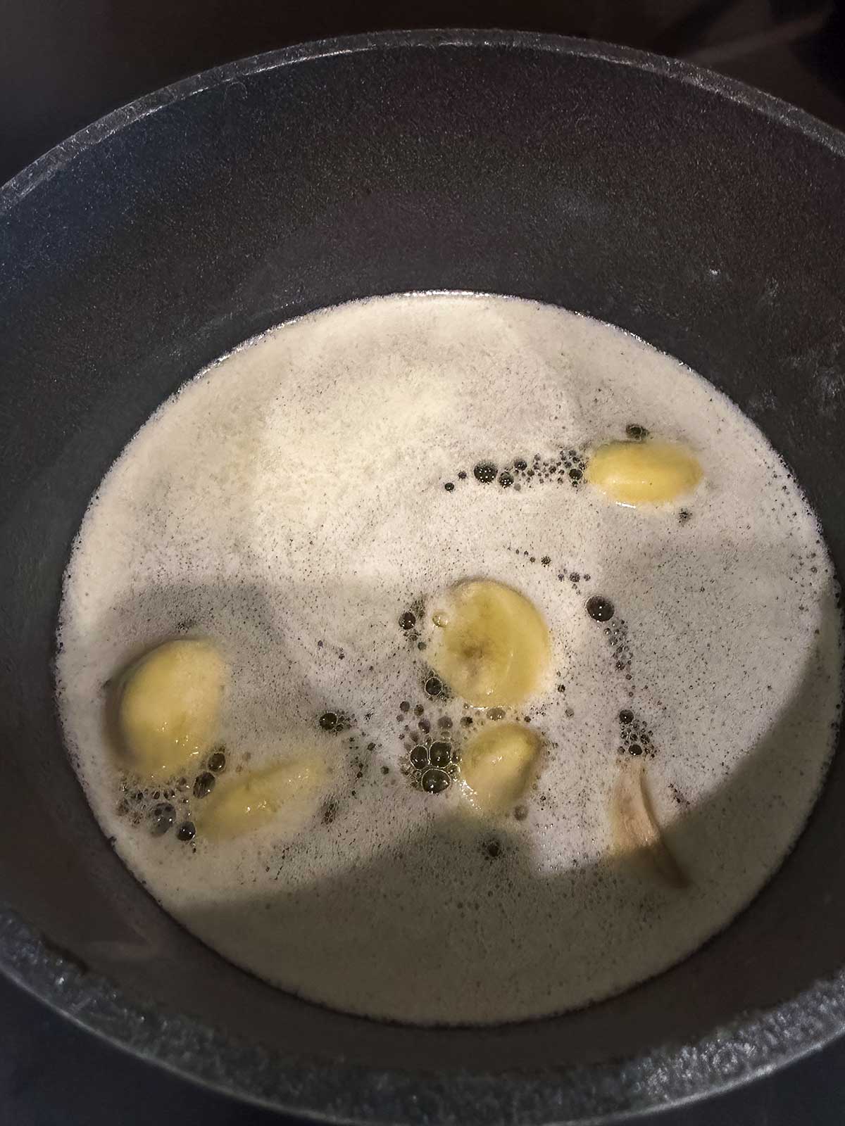 Sliced bananas boiling in a pot filled with foamy liquid, likely water or milk, seen from above.