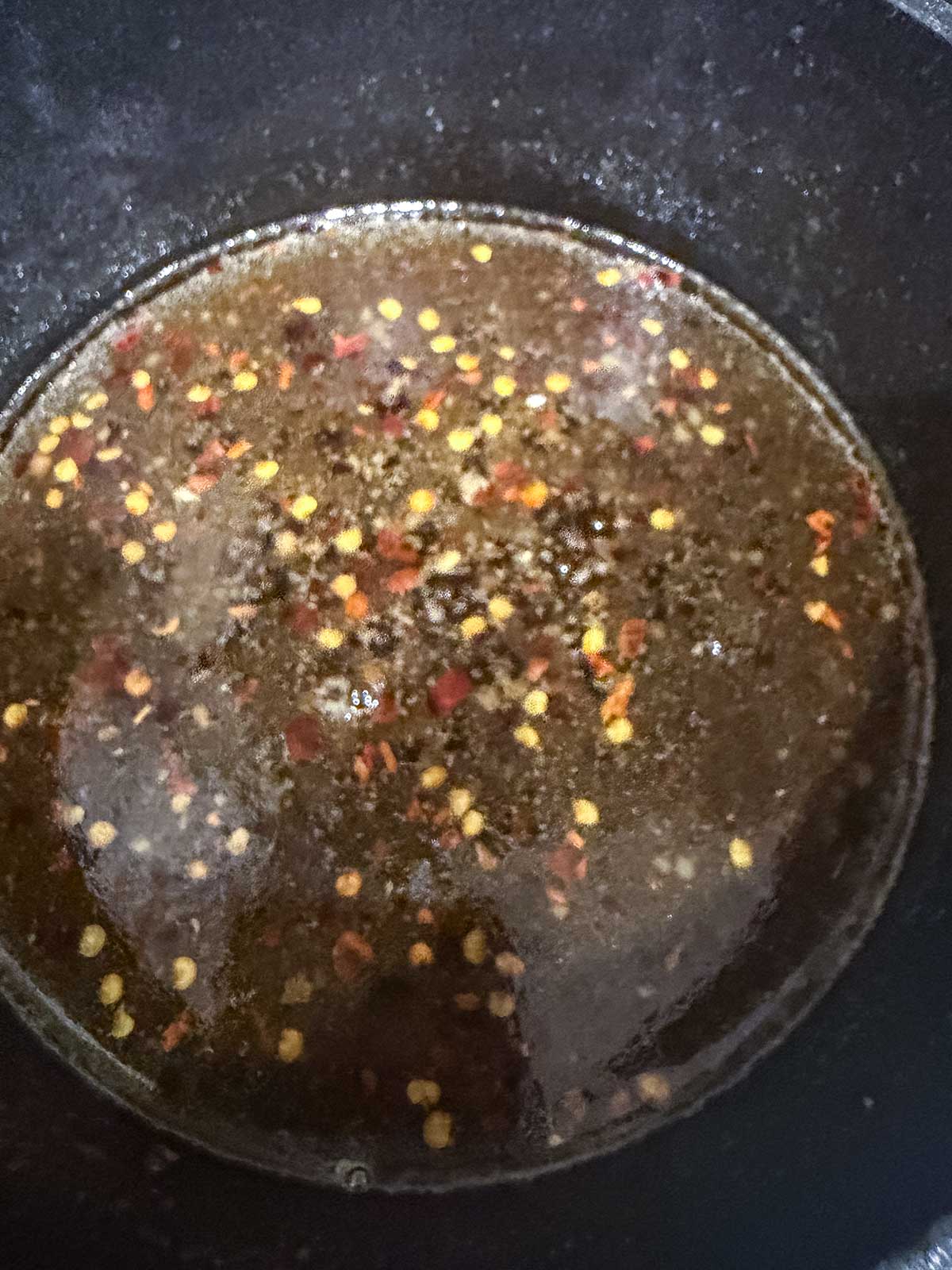 A close-up of a dark liquid with visible red chili flakes simmering in a black pot, perfect for glazing Honey Garlic Salmon or drizzling over crispy Air Fryer Salmon Bites.