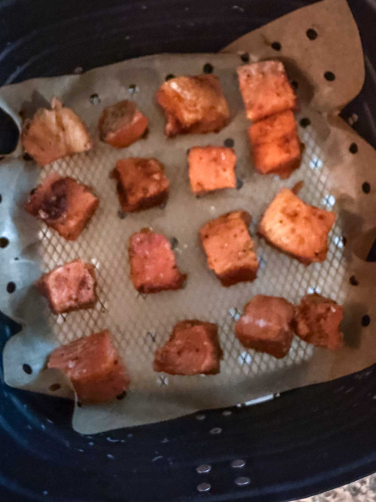 Cubed pieces of seasoned salmon, perfect for Honey Garlic Salmon bites, are arranged on parchment paper inside an air fryer basket, ready to be cooked or just cooked.