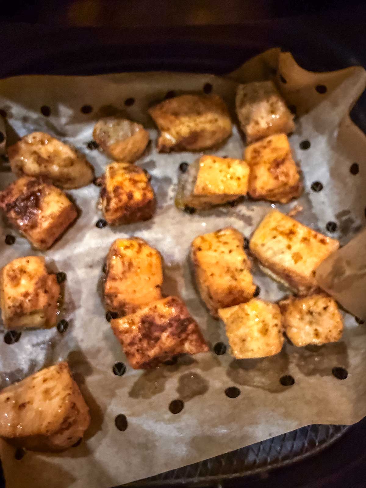 Golden brown cubes of seasoned salmon on parchment paper inside an air fryer basket, ready to be served—just like delicious air fryer salmon bites or honey garlic salmon.