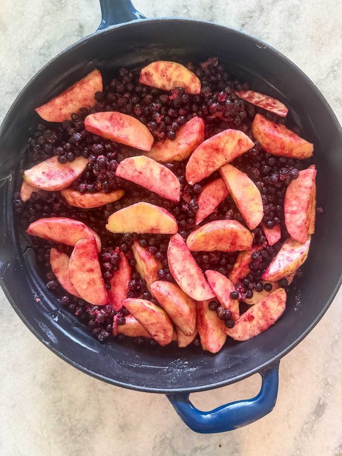 A blue baking dish filled with sliced peaches and blueberries coated in spices, reminiscent of an apple blueberry crisp, sits ready to be baked on a light-colored countertop.